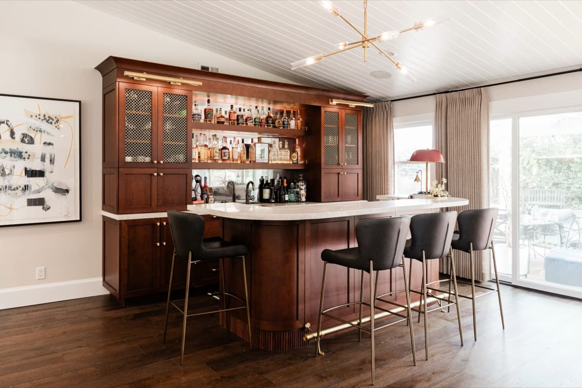 Custom walnut wet bar with antique brass metal-grille glass-front cabinets, fluted curved base